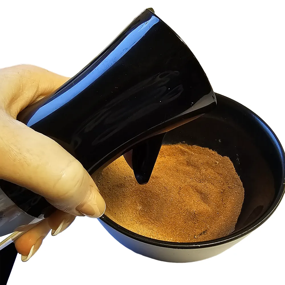 Hand hält schwarzes Dosiergerät/Spender über schwarze Schüssel mit feinem braunem Gewürzpulver (Zimt- oder Gewürzmischung)