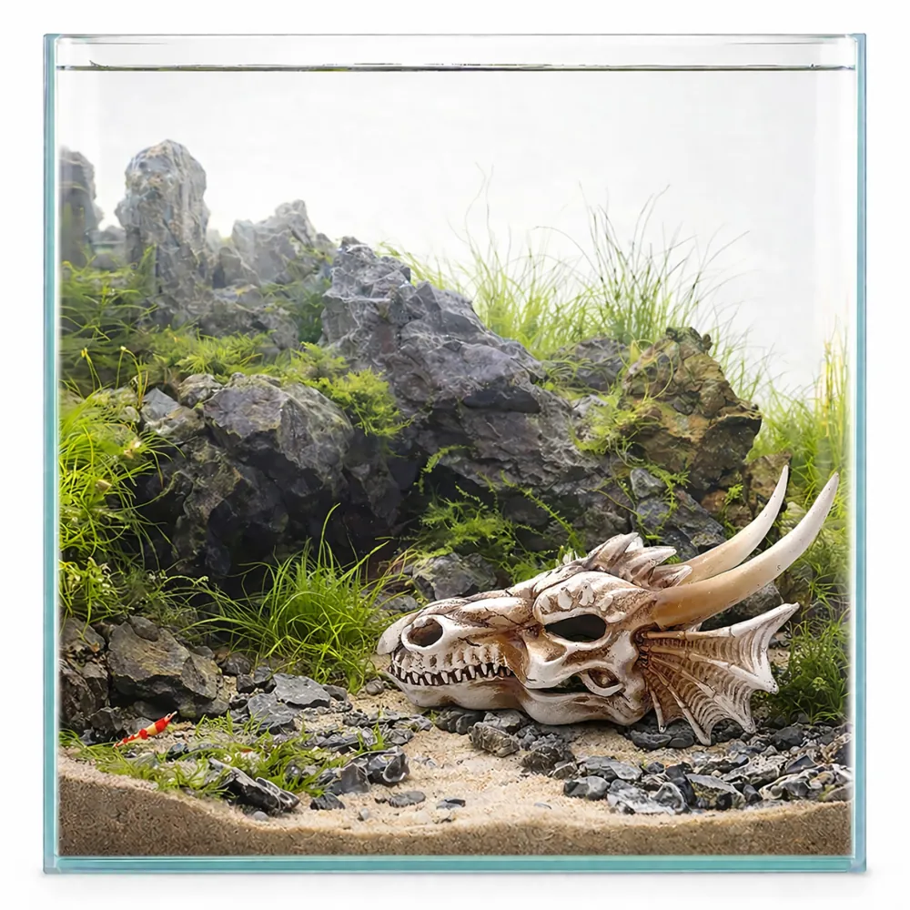 Drachen-Schädel Aquariumdeko auf Sandboden, umgeben von grauen Felsen, grünen Wasserpflanzen und kleinen Garnelen im Nano-Aquarium
