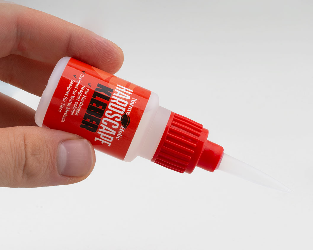Hand hält Flasche Hardscape-Kleber mit rotem Verschluss