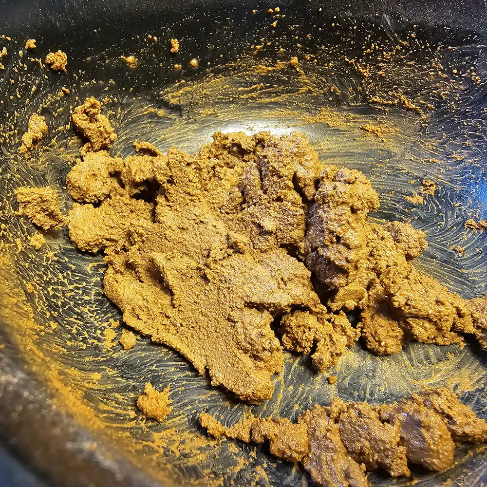 Nahaufnahme: gelblich-braunes Hobby Terrano Clay Powder (Lehmpulver) zu Klumpen angerührt in schwarzer Schüssel; zeigt Textur und Bindefähigkeit für formstabile Terrarien-Bodengründe