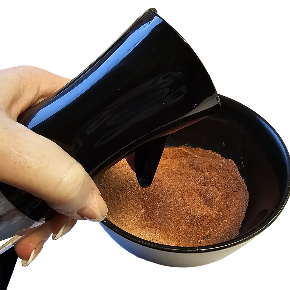Hand gießt Hobby Terrano Clay Powder rot (Lehmpulver) in schwarze Schale; fein gemahlenes, rein mineralisches Bindemittel für Terrarien-Bodengründe, Farbe rot, 1,3 kg